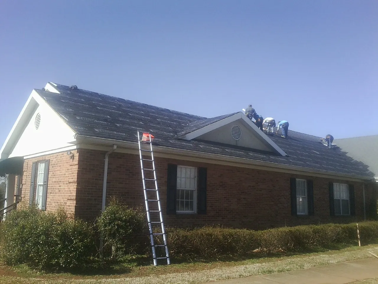 Crew tearing shingles off a brick ranch roof with a ladder set — Emergency Roof Repair work by our crew in Independence