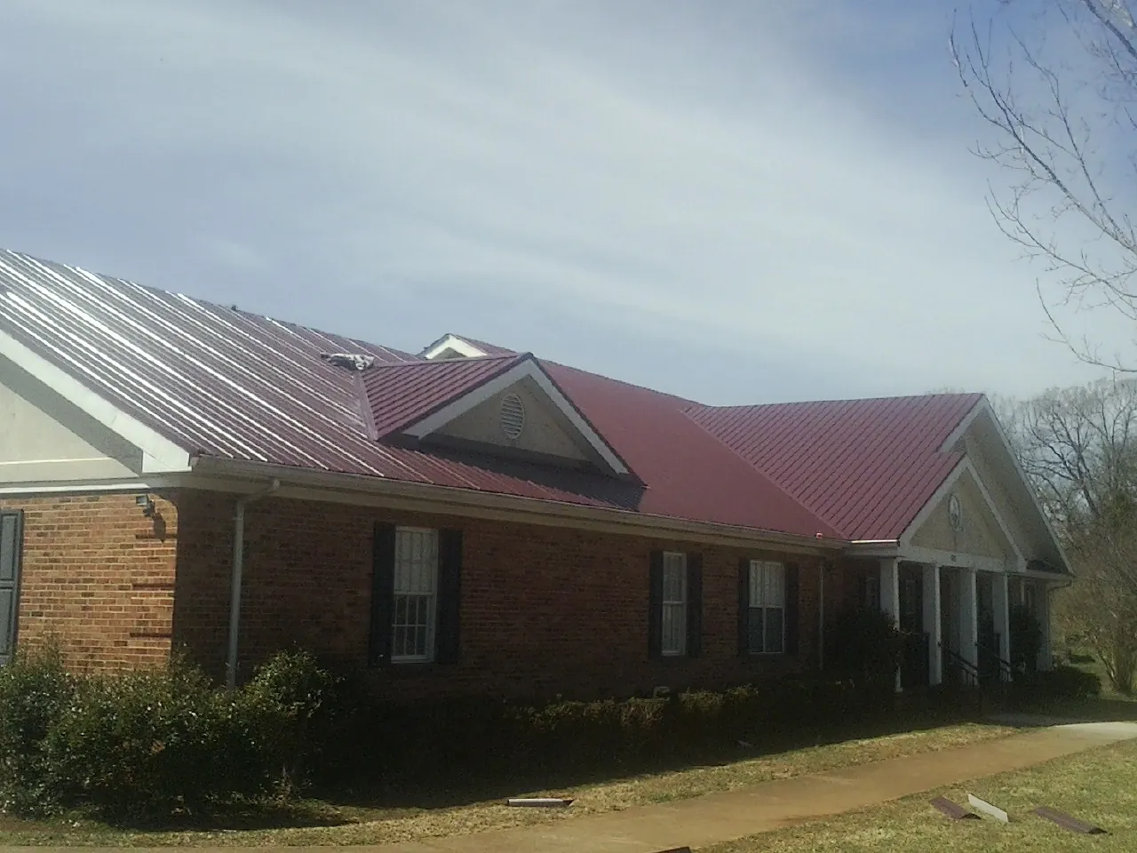 Red metal roof with gabled entries on a long brick building, from a Hail Damage Roof Repair job in Independence