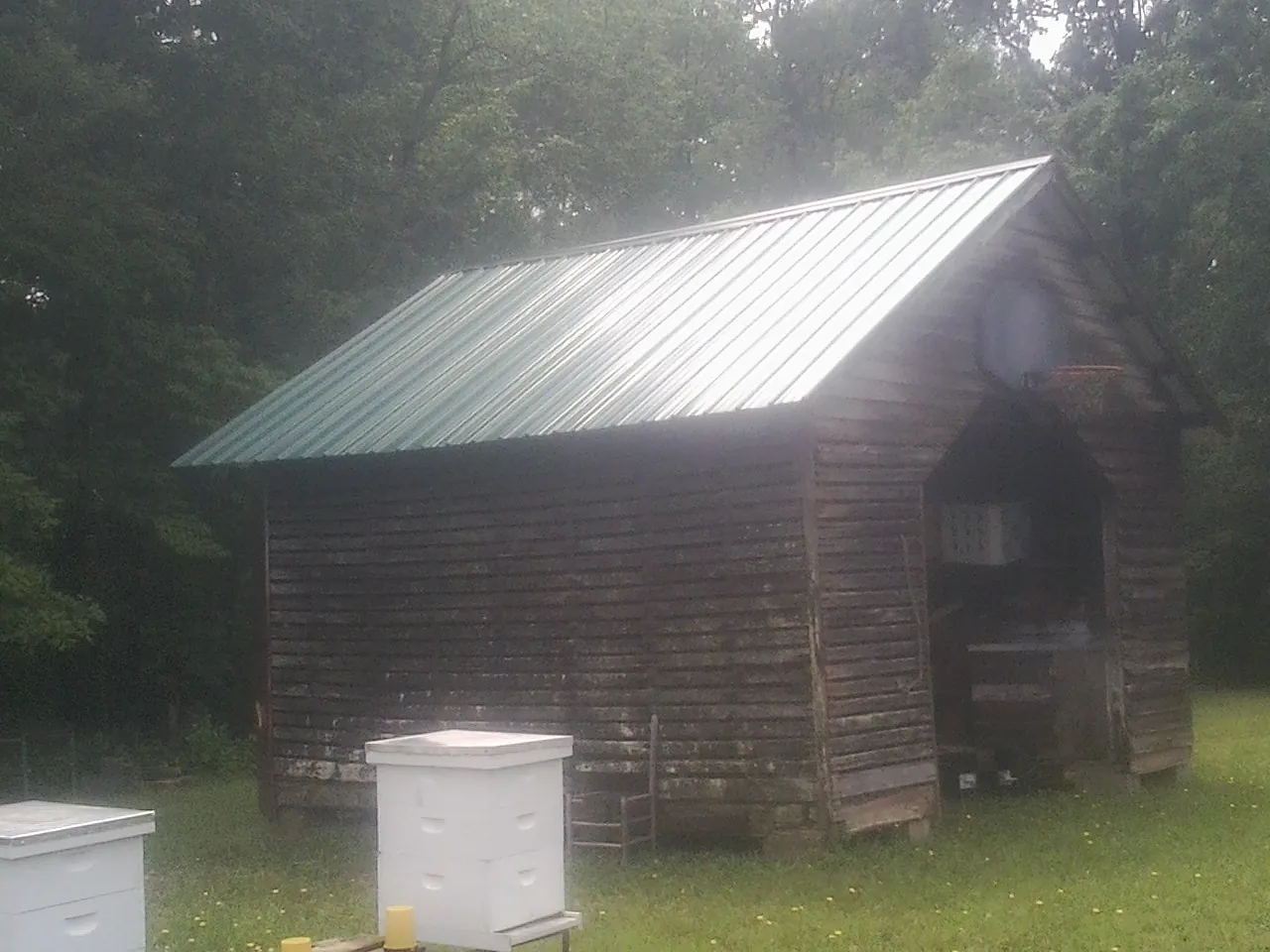 Green metal roof on a weathered barn beside stacked beehives in Independence